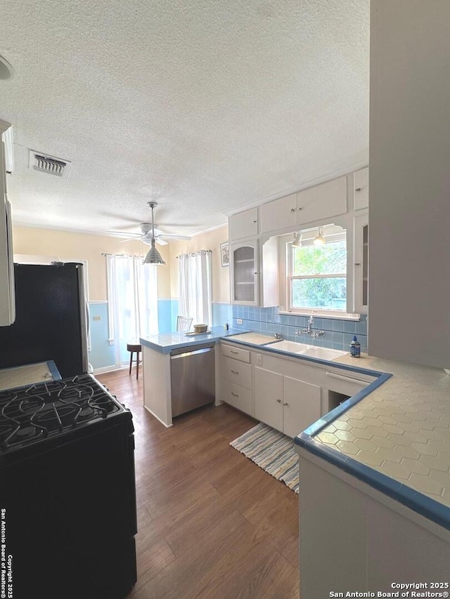 kitchen featuring a peninsula, a textured ceiling, visible vents, stainless steel appliances, and dark wood-style floors