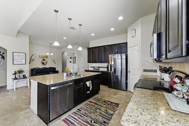 kitchen featuring backsplash, a center island with sink, appliances with stainless steel finishes, arched walkways, and a sink