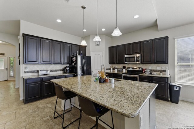 kitchen with a sink, a kitchen breakfast bar, light stone countertops, decorative backsplash, and stainless steel appliances