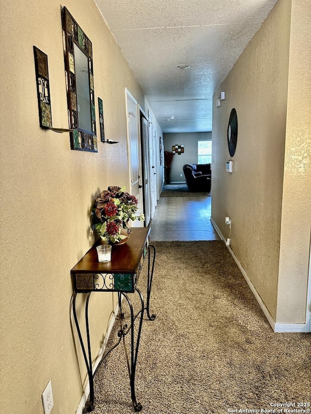 hallway with baseboards, carpet, a textured wall, and a textured ceiling