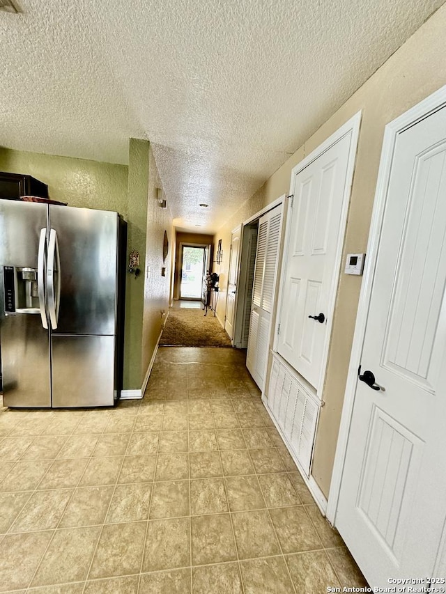 hall with a textured ceiling, baseboards, and light tile patterned flooring