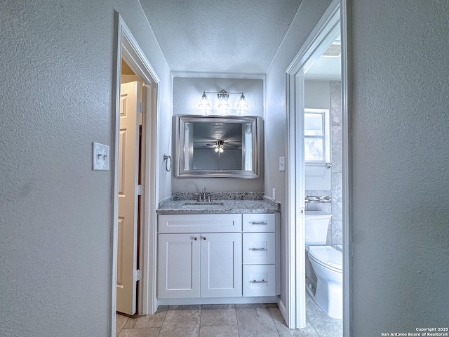 bathroom featuring toilet, vanity, a textured wall, and a textured ceiling