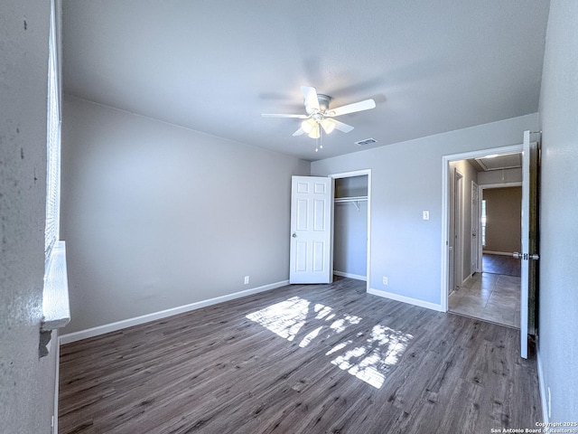 unfurnished bedroom featuring visible vents, baseboards, a closet, attic access, and wood finished floors