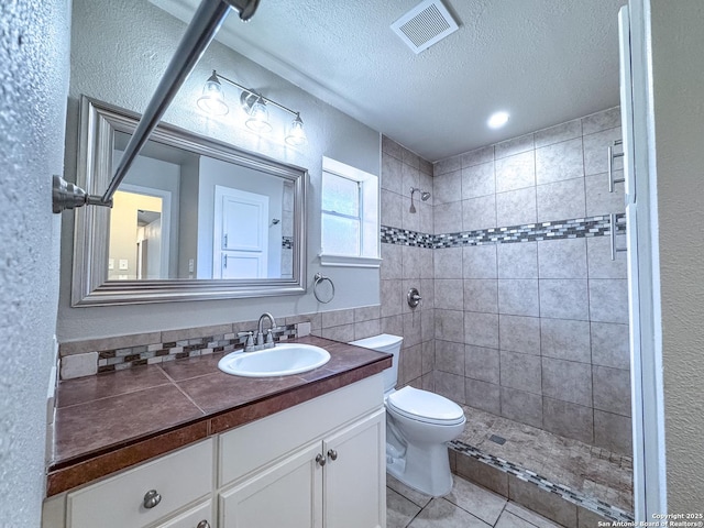 bathroom featuring a tile shower, a textured ceiling, vanity, visible vents, and toilet