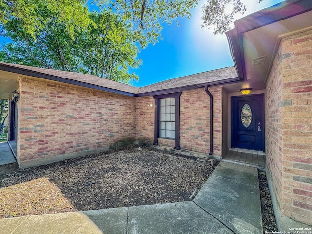 property entrance with brick siding and a shingled roof