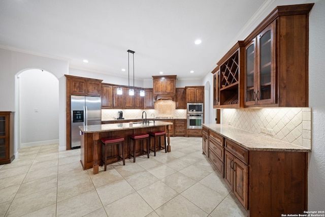 kitchen with tasteful backsplash, arched walkways, a sink, appliances with stainless steel finishes, and a kitchen breakfast bar