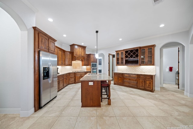 kitchen featuring tasteful backsplash, glass insert cabinets, arched walkways, a kitchen breakfast bar, and stainless steel appliances