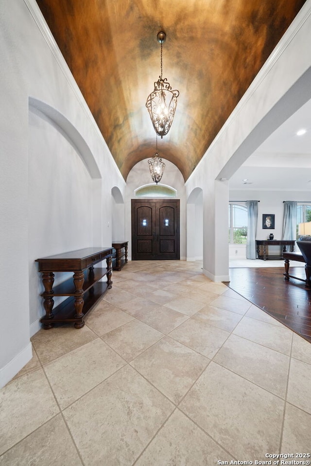 tiled entryway with arched walkways, baseboards, lofted ceiling, and a notable chandelier