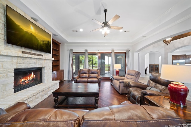 living area with ceiling fan, a fireplace, a tray ceiling, arched walkways, and hardwood / wood-style floors