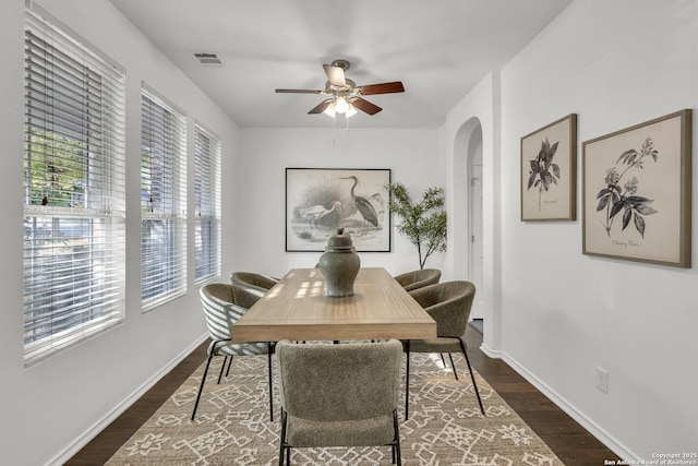 dining area featuring visible vents, baseboards, arched walkways, a ceiling fan, and dark wood-type flooring
