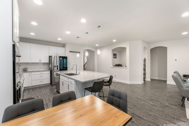 kitchen with baseboards, arched walkways, a sink, open floor plan, and recessed lighting
