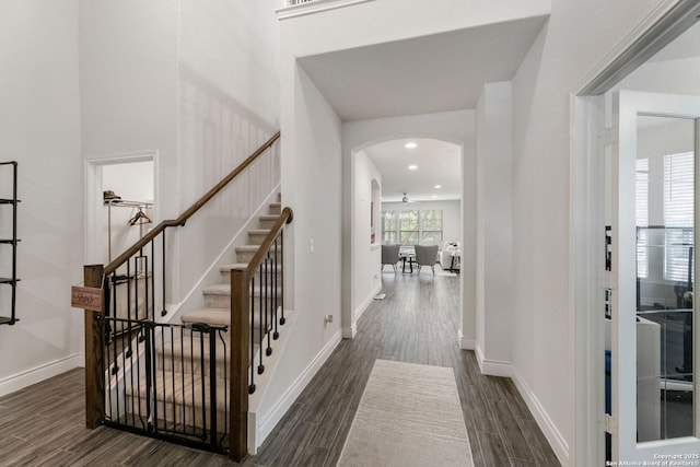 foyer entrance featuring dark wood-type flooring, arched walkways, and stairway