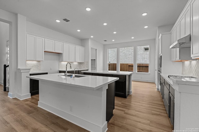 kitchen featuring a sink, ventilation hood, a kitchen island with sink, visible vents, and recessed lighting
