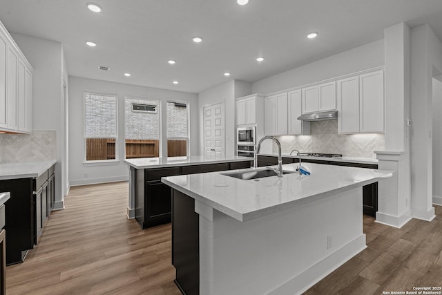 kitchen with a sink, recessed lighting, an island with sink, under cabinet range hood, and appliances with stainless steel finishes