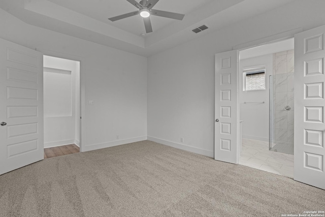 carpeted empty room featuring a ceiling fan, a raised ceiling, baseboards, and visible vents