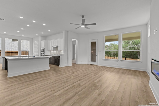 unfurnished living room with a ceiling fan, light wood-style flooring, recessed lighting, baseboards, and a sink