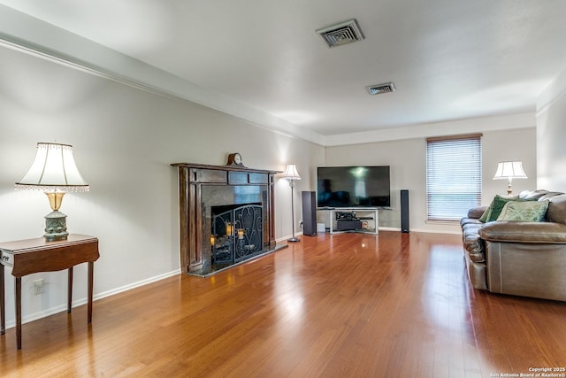 living area featuring baseboards, a fireplace with raised hearth, wood finished floors, and visible vents