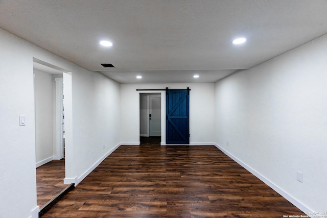 empty room with visible vents, baseboards, a barn door, dark wood finished floors, and recessed lighting