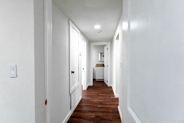 hallway with dark wood-type flooring, visible vents, baseboards, and a textured wall