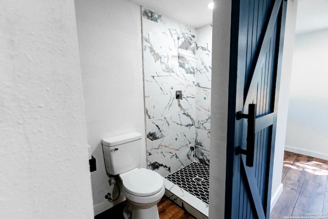 bathroom with toilet, wood finished floors, a stall shower, a textured wall, and baseboards