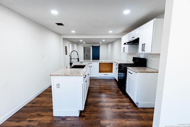 kitchen with light stone countertops, under cabinet range hood, a sink, backsplash, and black gas range oven