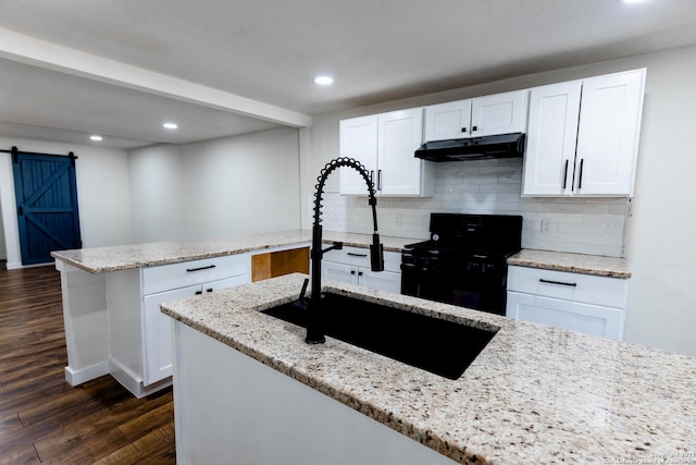 kitchen featuring black range with gas cooktop, a barn door, a sink, dark wood finished floors, and under cabinet range hood