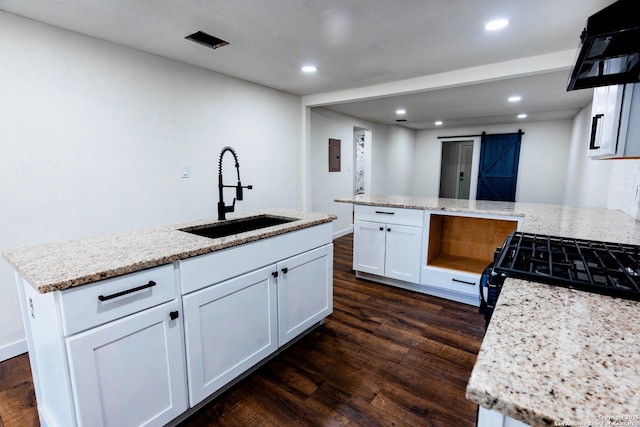 kitchen with dark wood-type flooring, white cabinets, a barn door, a sink, and extractor fan