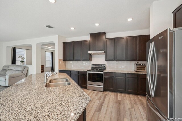 kitchen with under cabinet range hood, visible vents, stainless steel appliances, arched walkways, and a sink