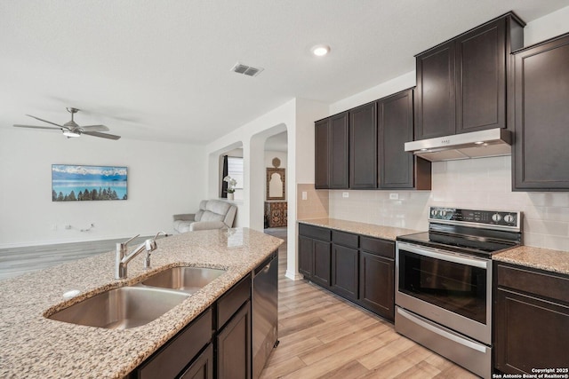 kitchen featuring arched walkways, under cabinet range hood, a sink, stainless steel appliances, and light wood finished floors
