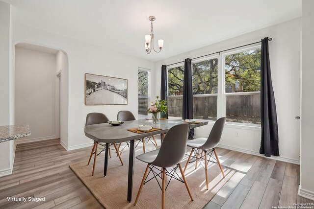 dining room with light wood-style flooring, arched walkways, a notable chandelier, and baseboards