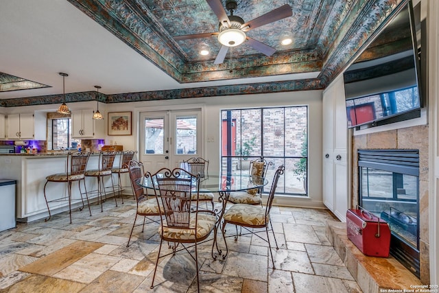 527 Thelma Dr, Olmos Park, TX 78212 - dining area with baseboards, a tiled fireplace, a ceiling fan, a tray ceiling, and stone tile floors