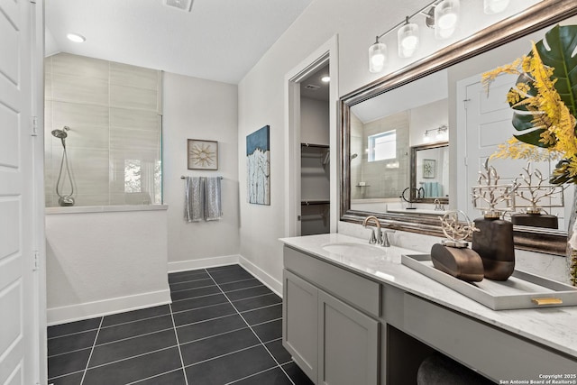 bathroom featuring vanity, baseboards, tile patterned flooring, a walk in closet, and a tile shower