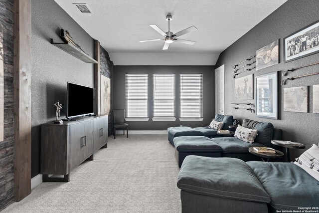 living room with a textured wall, visible vents, light carpet, and ceiling fan