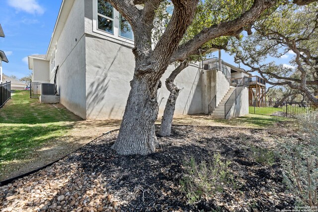 view of side of property with central air condition unit, a yard, stucco siding, fence, and stairs
