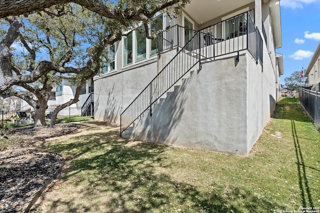 view of home's exterior featuring a lawn, stucco siding, fence, and stairway