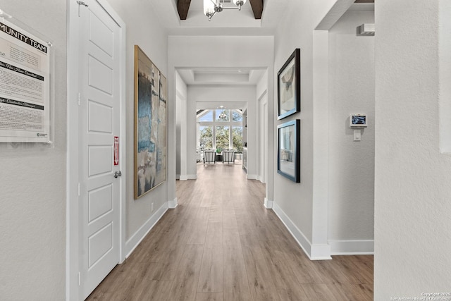 hall featuring a textured wall, baseboards, and wood finished floors