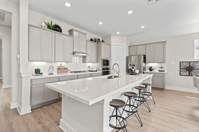 kitchen featuring a kitchen breakfast bar, gray cabinets, under cabinet range hood, appliances with stainless steel finishes, and a sink