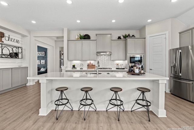 kitchen featuring stainless steel fridge with ice dispenser, a sink, under cabinet range hood, light wood finished floors, and built in microwave