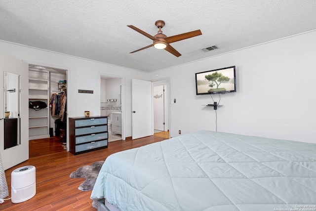 296 Wolf Ln, La Vernia, TX 78121 - bedroom featuring visible vents, a textured ceiling, a walk in closet, ensuite bath, and wood finished floors