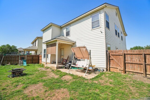 rear view of house with a fire pit, a patio area, a lawn, a fenced backyard, and a gate