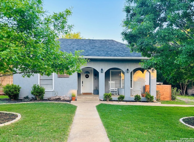 view of front of home featuring stucco siding, roof with shingles, a porch, and a front yard