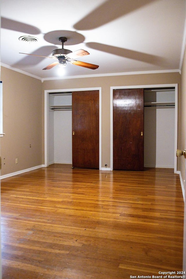 unfurnished bedroom with crown molding, visible vents, multiple closets, and wood finished floors