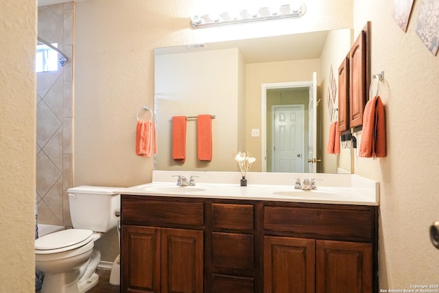 full bath featuring a textured wall, double vanity, a sink, and toilet