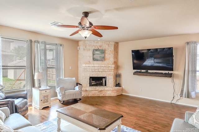 living room featuring light wood-type flooring, a ceiling fan, a stone fireplace, visible vents, and baseboards