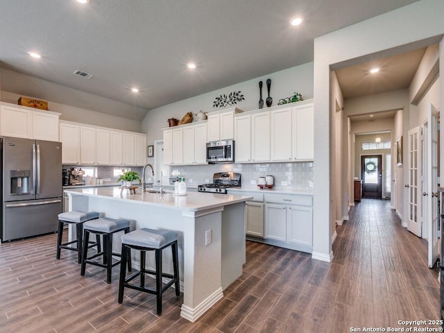 kitchen featuring visible vents, a sink, an island with sink, stainless steel appliances, and dark wood-type flooring
