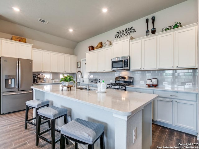 kitchen featuring vaulted ceiling, visible vents, appliances with stainless steel finishes, a sink, and wood finished floors