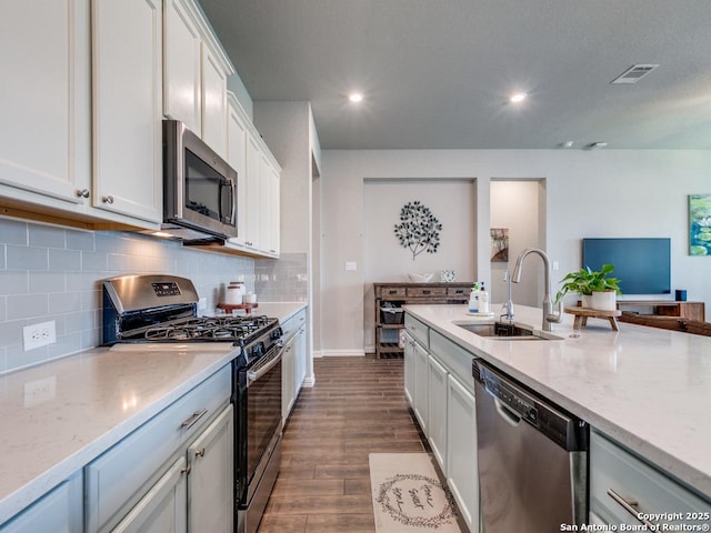 kitchen featuring white cabinets, light stone counters, a sink, stainless steel appliances, and dark wood-style floors