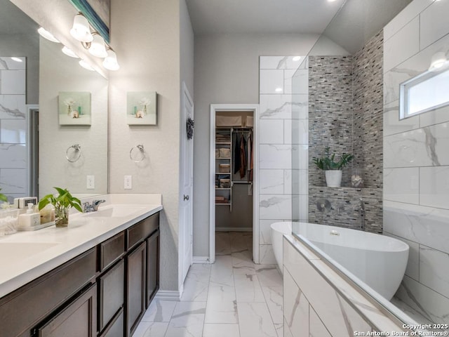 full bath with a spacious closet, marble finish floor, a sink, a freestanding bath, and double vanity