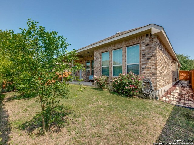 view of property exterior featuring brick siding, fence, a yard, and a patio