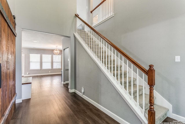 stairs featuring a chandelier, a barn door, baseboards, and wood finished floors